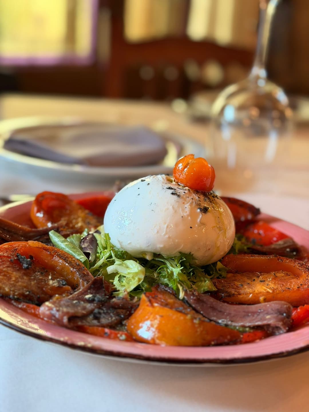 Burrata con tomates, pimientos asados y anchoas servida para compartir.